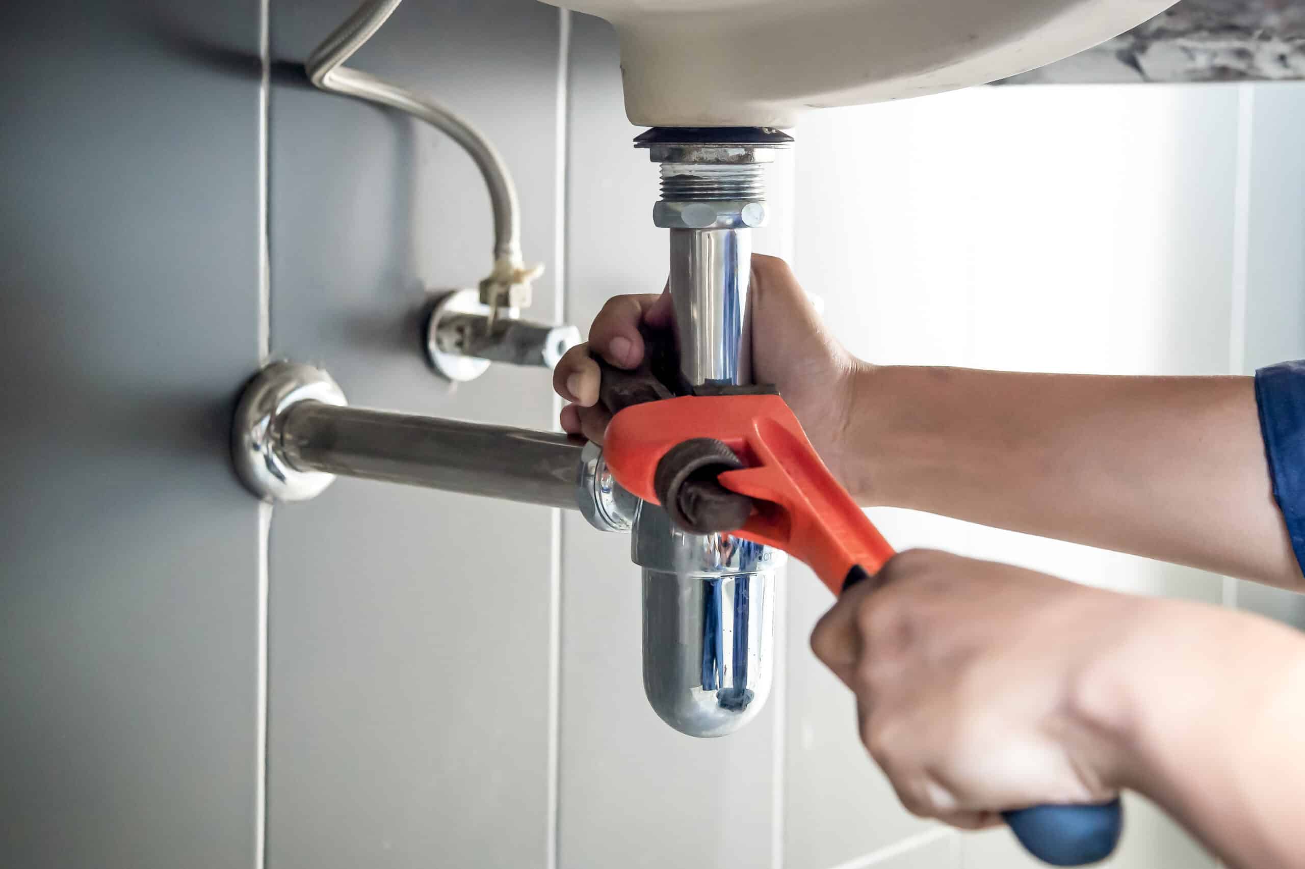 Plumber using a wrench to repair and clean a clogged drain under a sink