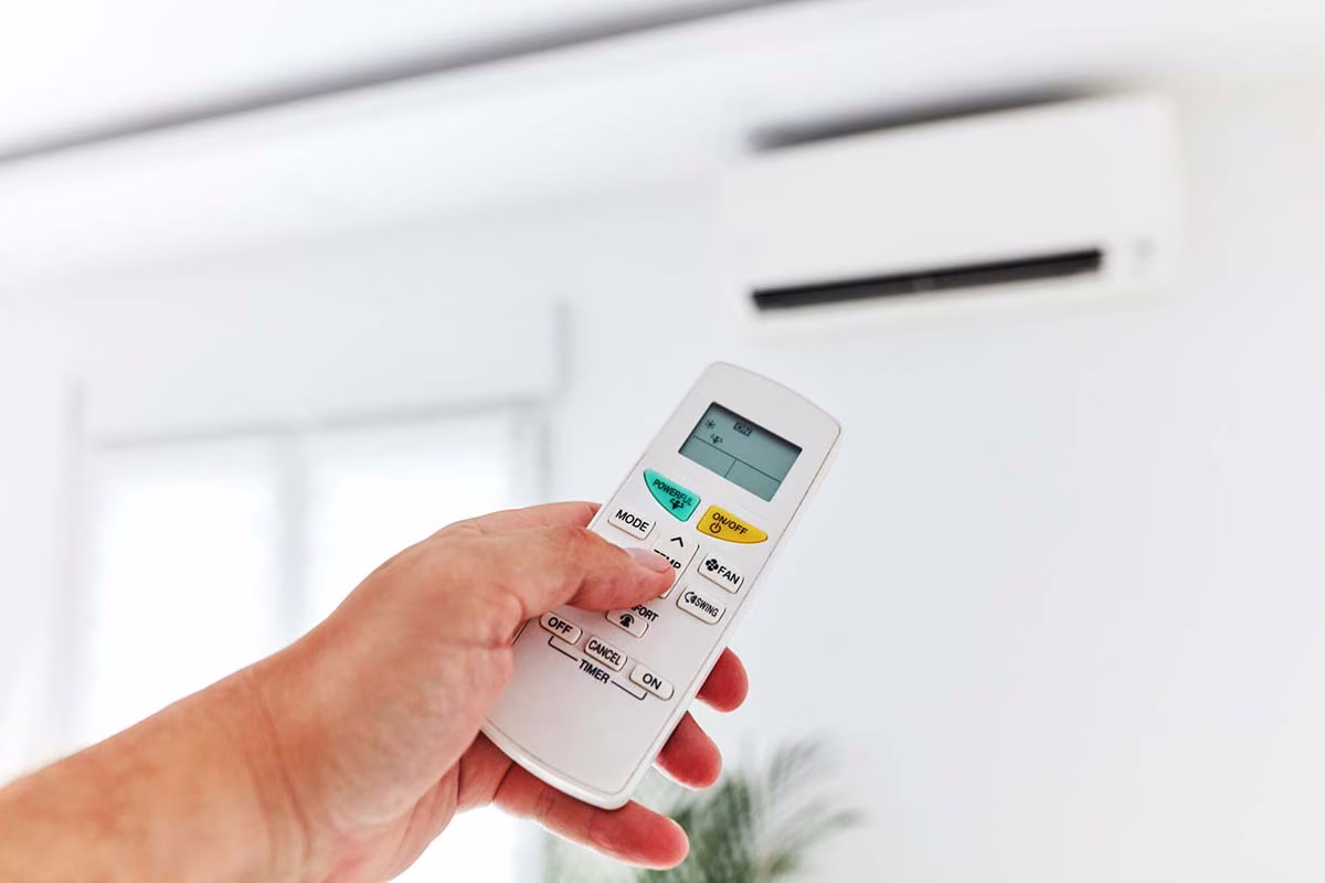 Hand pointing a remote control at a wall mounted mini split unit