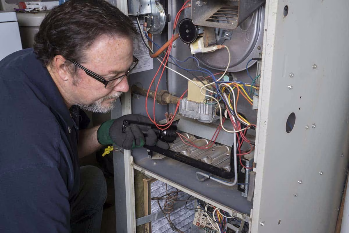 Technician working inside an open furnace during a heating and cooling service