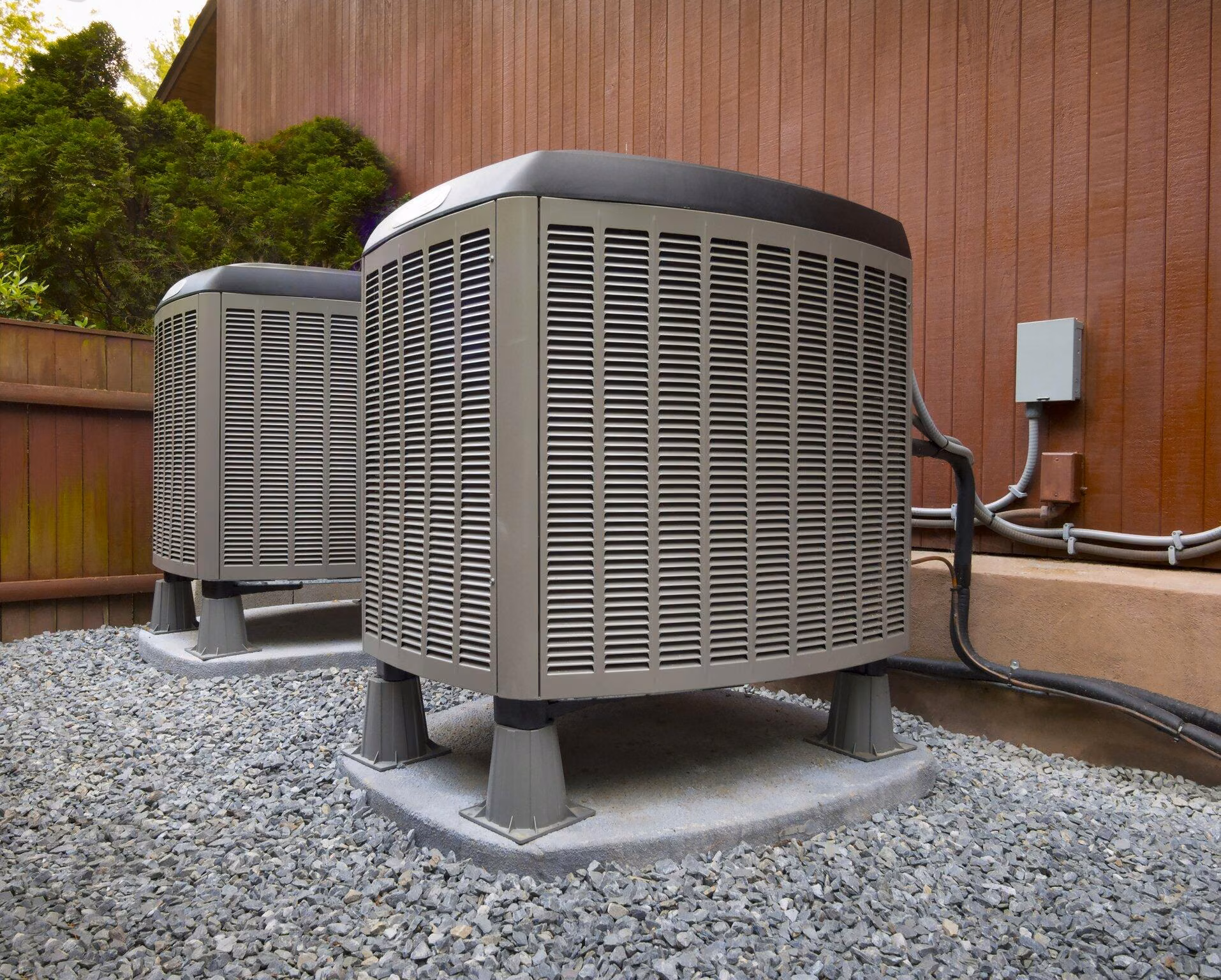 Two outdoor HVAC units on a pad beside a fence ready for preventative maintenance