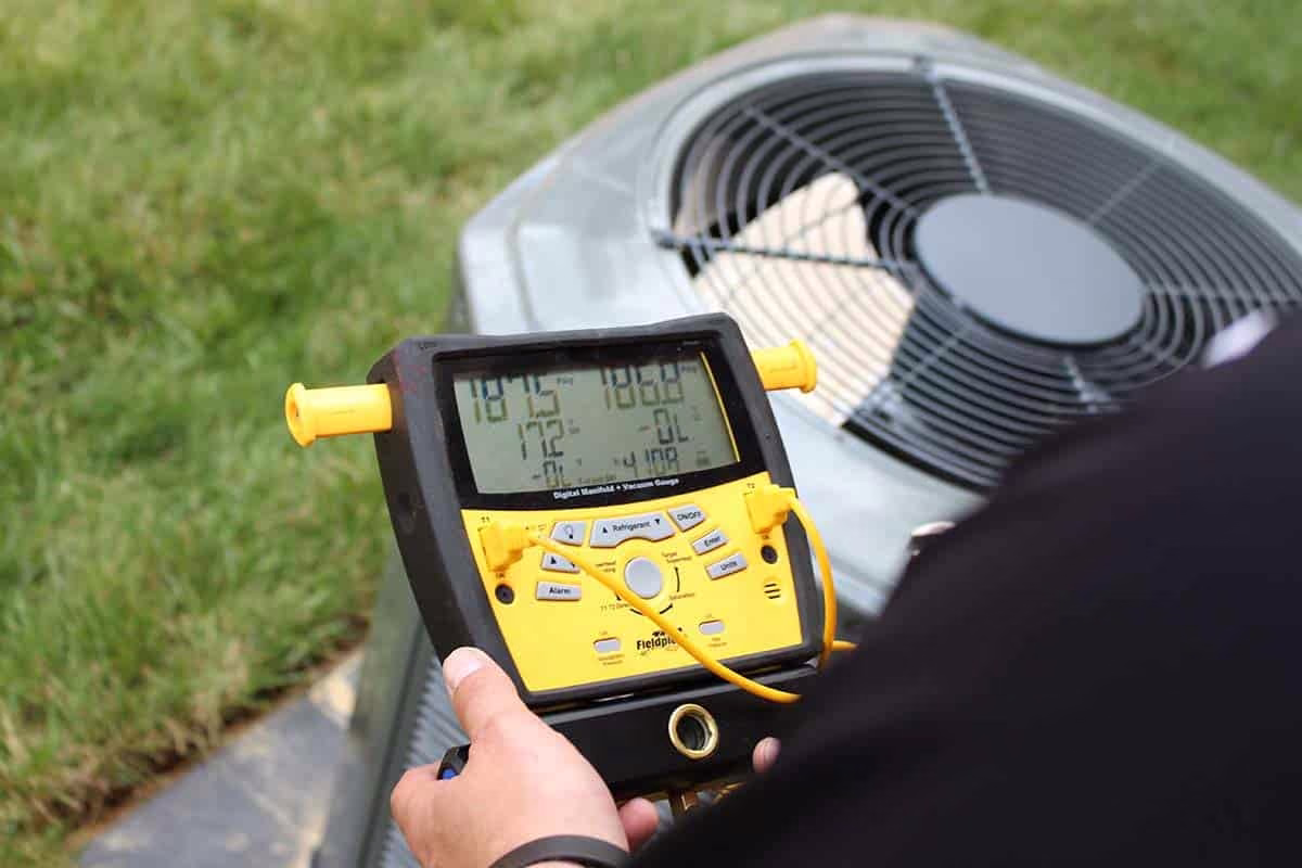HVAC technician reading a digital manifold gauge while diagnosing an air conditioner