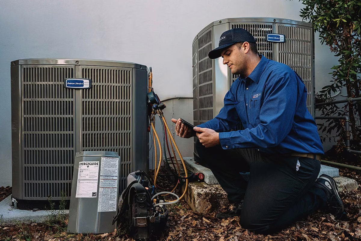 Technician kneeling with a tablet to inspect two outdoor heating and cooling units