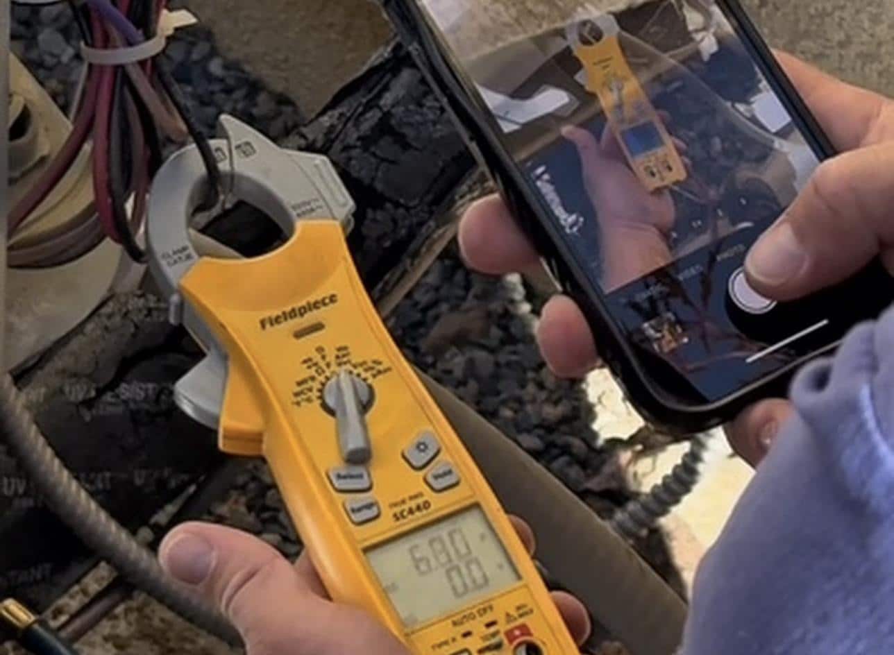 Technician logging a clamp meter amp reading during an HVAC tune-up