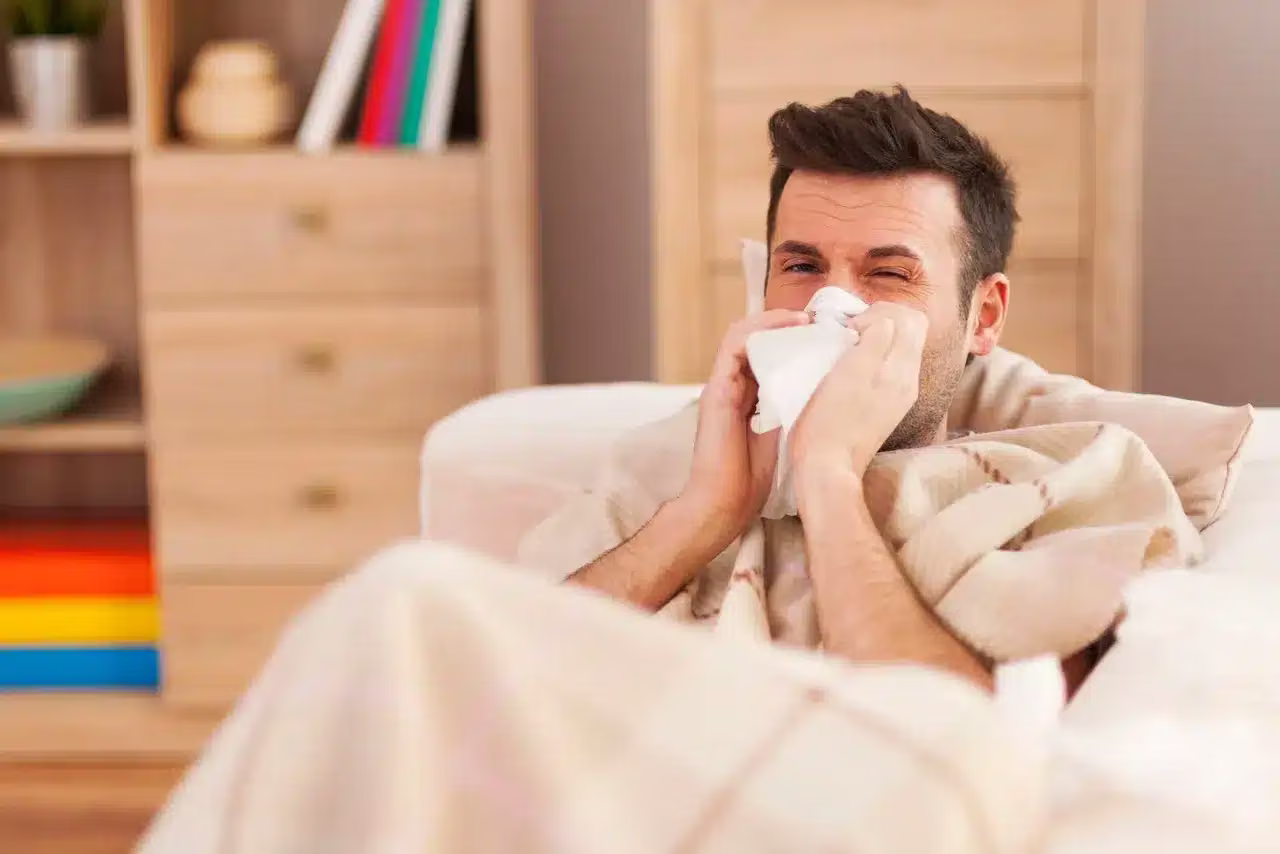 Man sneezing into a tissue indoors while sitting on a couch