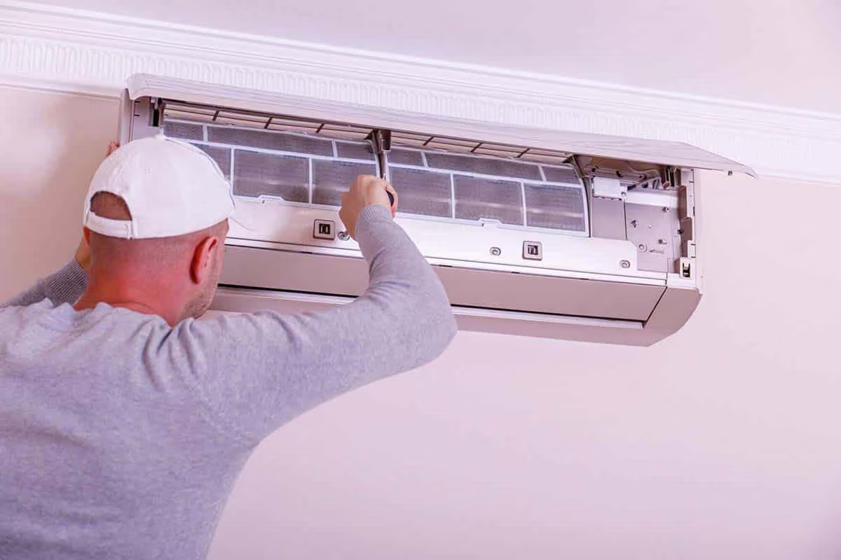 Man opening the cover of a ductless mini split to inspect the unit