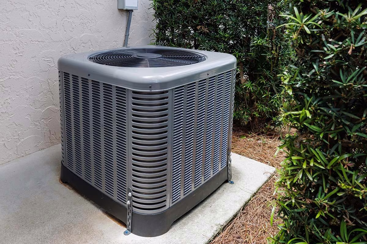 Outdoor air conditioner condenser unit on a pad beside a stucco home