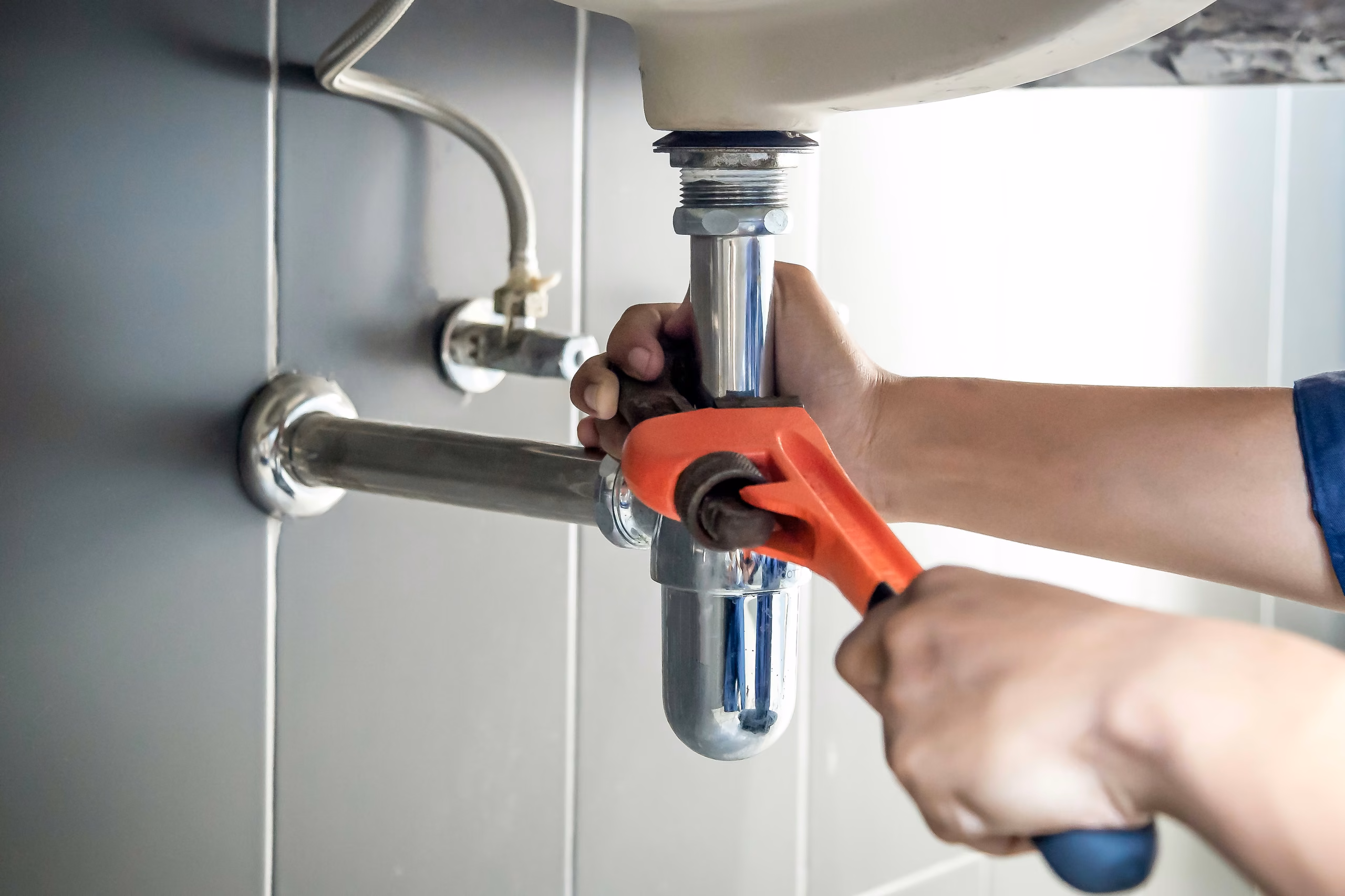 Plumber using a wrench on a sink drain trap during a Sacramento drain cleaning