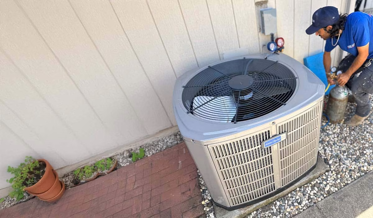 Technician with a refrigerant tank repairing a leak at an outdoor air conditioner