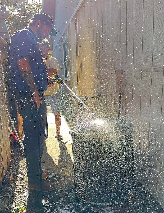 American Energy technician rinsing a condenser coil with a water hose