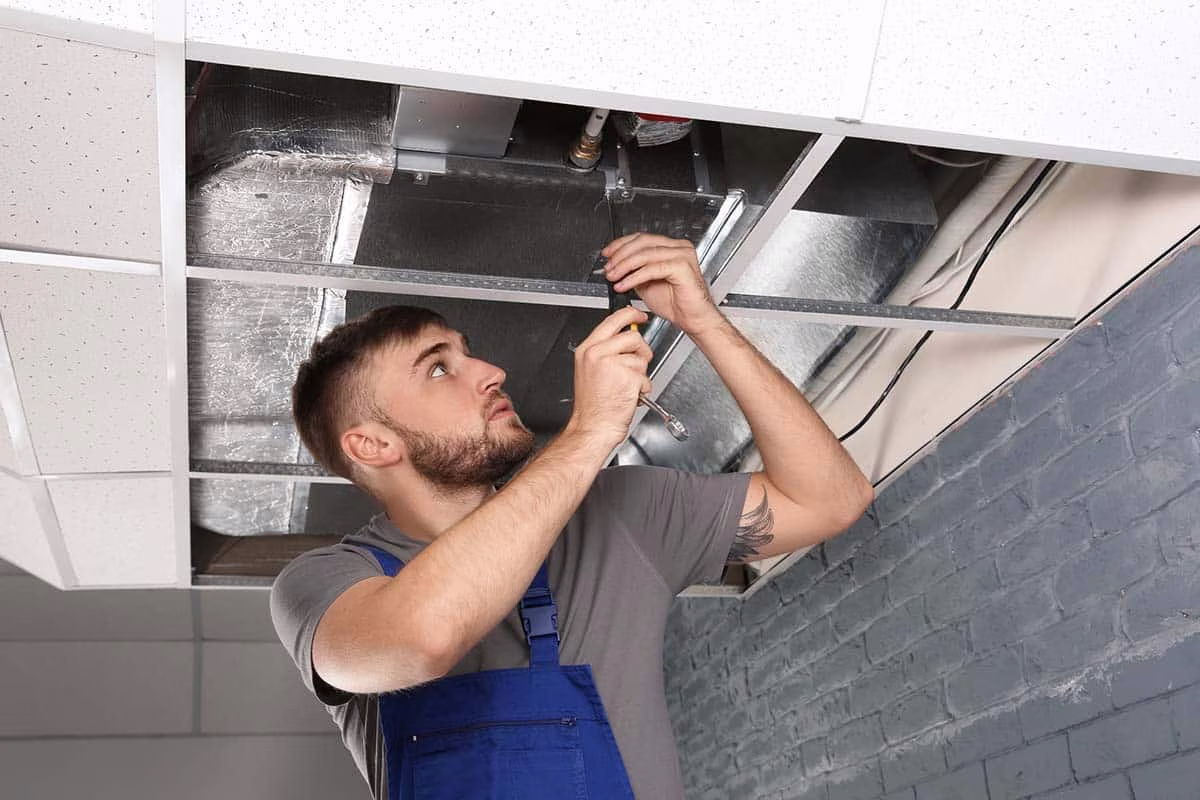 Technician working on exposed ceiling ductwork during an air duct service
