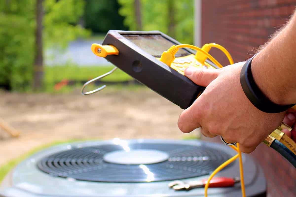 Technician holding a tablet above an outdoor air conditioner during an inspection