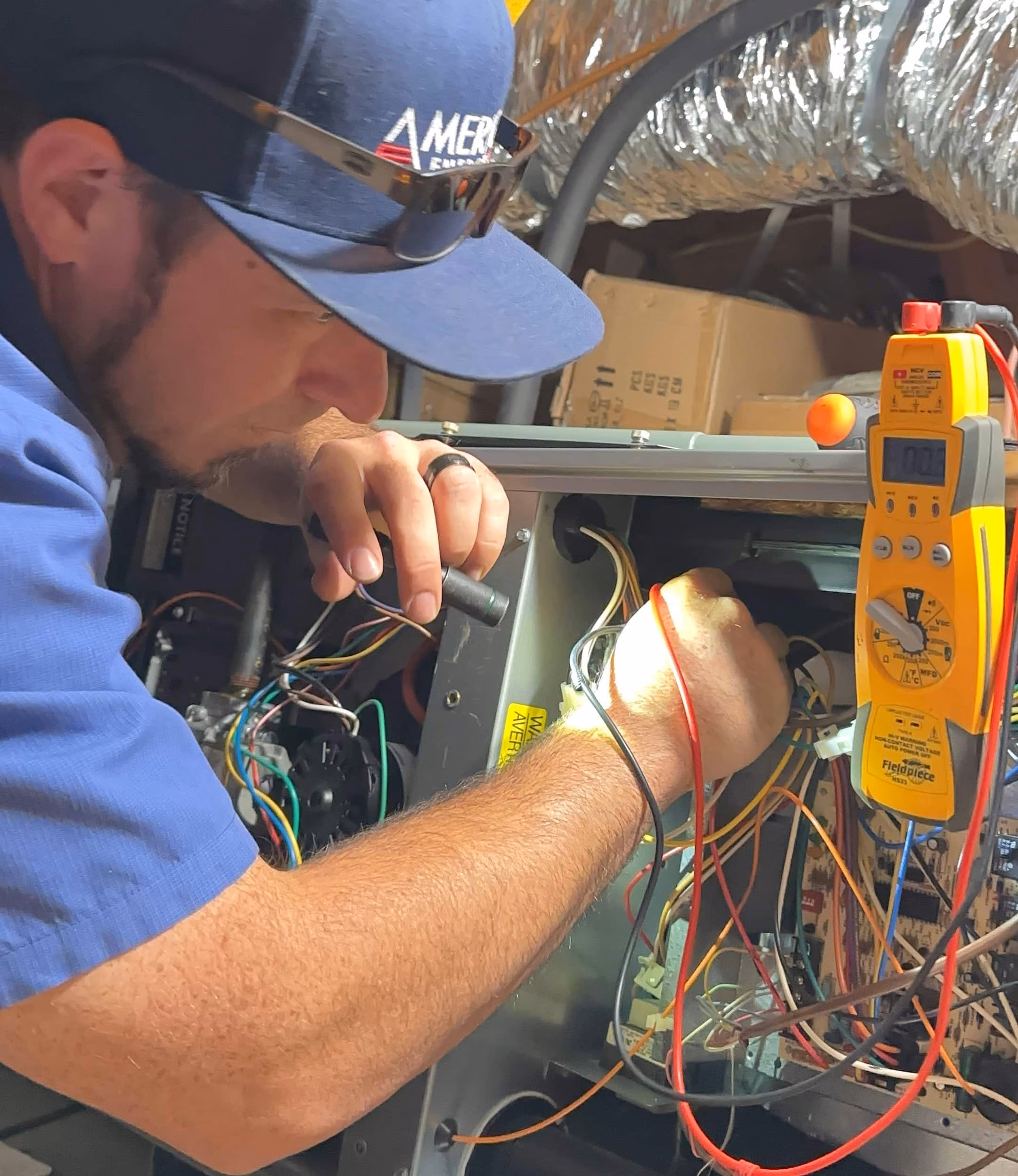 American Energy technician testing HVAC wiring with a meter in an attic