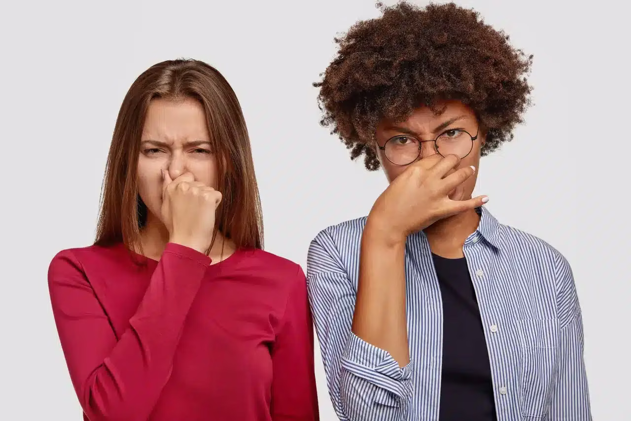 Two people pinching their noses at an unpleasant odor indoors